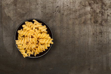 Fusilli in a black bowl on a metal table in a top viewの写真素材