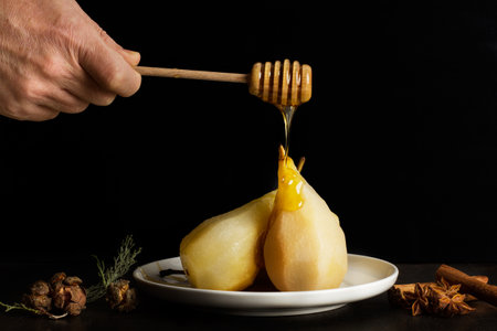 Man hand dripping honey on baked pears on a white plate in a dark backgroundの写真素材