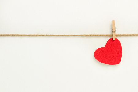 A red paper heart hanging from a sisal yarn on white backgroundの写真素材