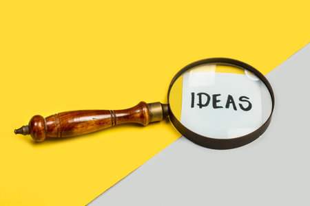 A magnifying glass and ideas word write on a paper on a yellow and gray backgroundの写真素材