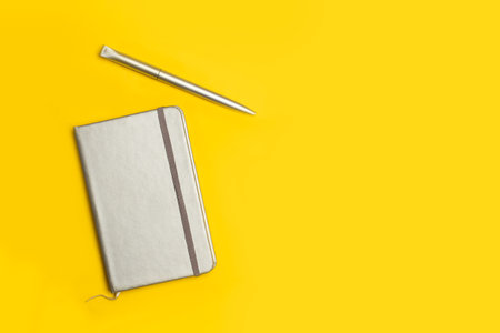 A gray diary and a pen on a yellow background with copy spaceの写真素材