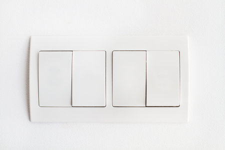 Four white light switches on a white wall in a close up view