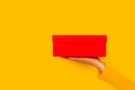 Woman hand holding a red box on a yellow background with copy spaceの写真素材