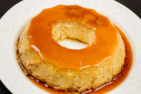 An eggs flan on a white ceramic plate on a black background in a top viewの写真素材