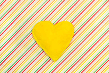 Yellow textile heart on a colored striped backgroundの写真素材