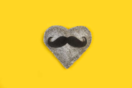 A gray textile heart with a black mustache on a yellow backgroundの写真素材