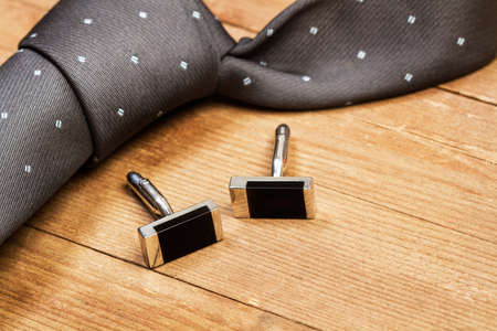 A gray tie and black cufflinks on a wooden table