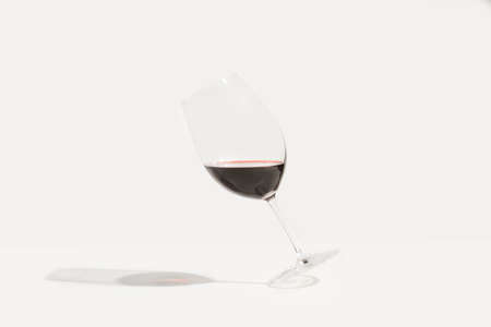 A tilted glass of red wine on a white backgroundの写真素材