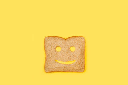 A slice of wholemeal bread with a face shape on a yellow backgroundの写真素材