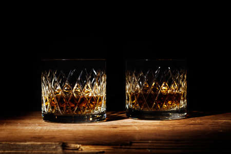 Two glasses of whiskey on a wooden table on a dark background