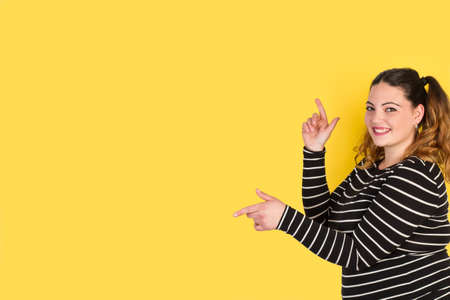 Curvy woman smiling and pointing wih her fingers on a yellow backgroundの写真素材