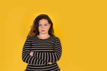 Curvy woman with angry face and crossed arms on a yellow backgroundの写真素材