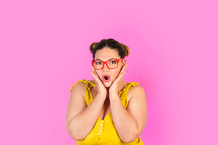 Curvy woman with hands on her face and surprised gesture on a pink backgroundの写真素材