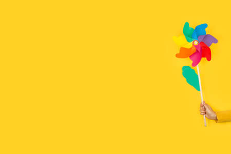 Woman hand holding a colored big pinwheel on a yellow background with copy space