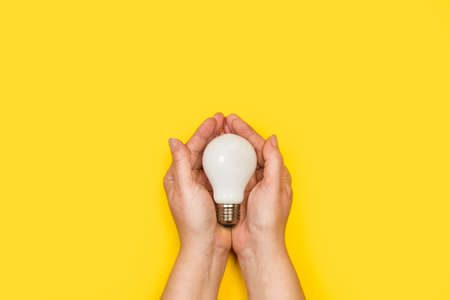Woman holding with both hands a lightbulb on a yellow background