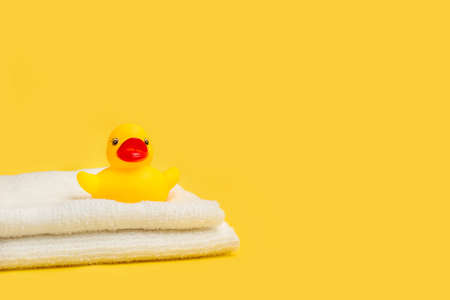A yellow rubber toy duck on white towels and on a yellow background