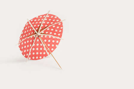 A red with white dots open cocktail umbrella on a white background