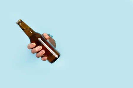 Man hand holding a bottle of beer through a hole in a light blue backgroundの写真素材