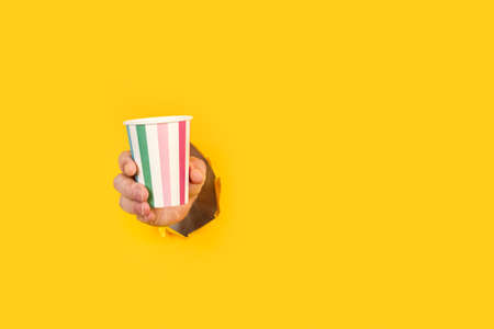 Man holding a striped party glass through a hole in a yellow background