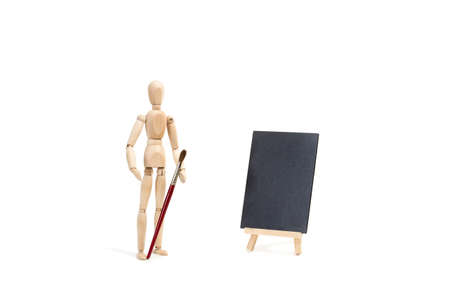 A wooden manequin toy with a paintbrush in his hand on white background