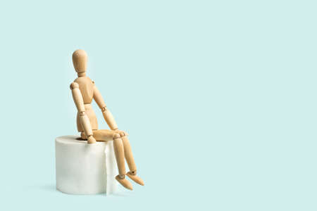 A wooden mannequin toy sitting on a roll of toilet paper on a white backgroundの写真素材