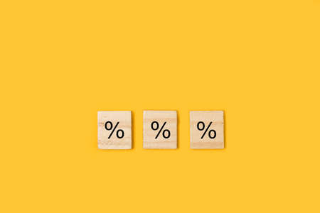 Percentage sign in wooden letter blocks on a yellow backgroundの写真素材