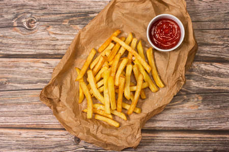 Fried potatoes and a bowl with ketchup on a wooden table