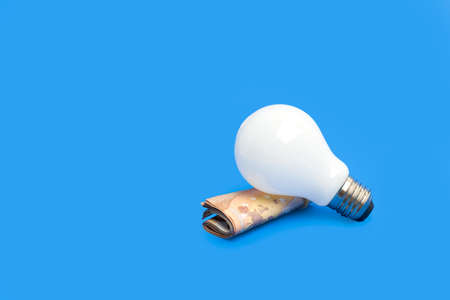 Lightbulb over a roll of euro bills on a blue backgroundの写真素材