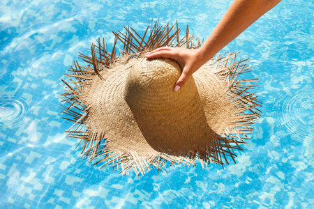 hand holding a straw hat on a swimming pool background