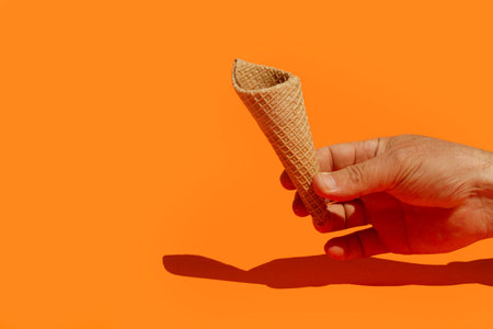Man hand holding a wafer cone on an orange backgroundの写真素材