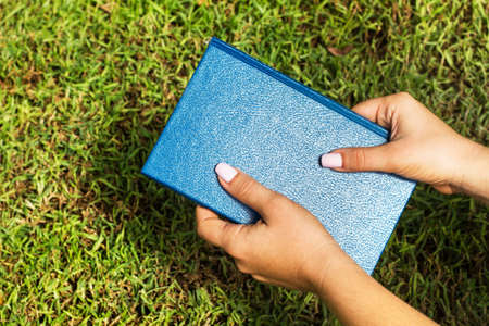 Woman hands holding a blue closed book on the grassの写真素材