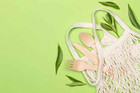 Wooden cutlery in a cotton mesh bag on a green background