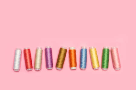 Colored thread spools on a pink background in a top view