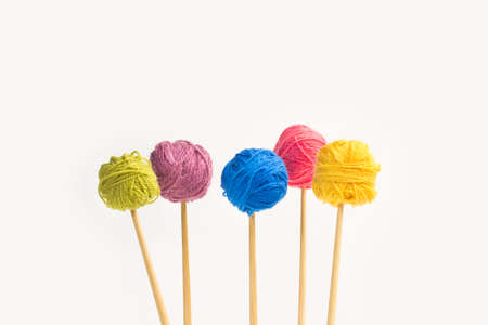 Colored wool balls on knitting needles on a white background