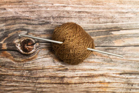 Brown wool spool and a crochet needle on a wooden background