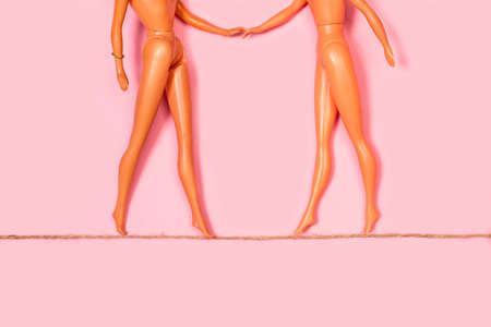 Two naked dolls walking on a rope and holding hands on a pink backgroundの写真素材
