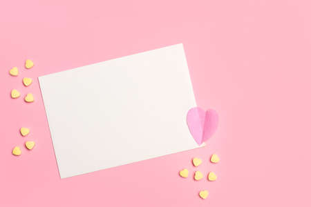 A blank white paper card with copy space and yellow candy hearts on a pink backgroundの写真素材