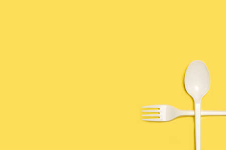Disposable white plastic fork and spoon on a yellow background with copy spaceの写真素材