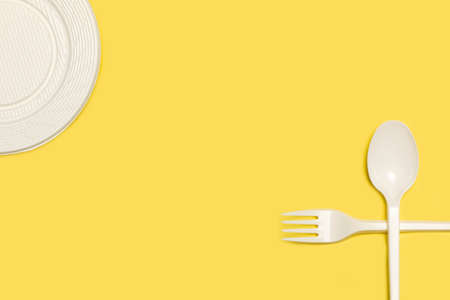 Disposable white plastic for, spoon and plate on a yellow background with copy space