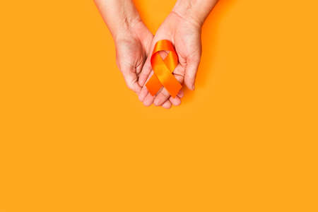 Woman hand holding an orange ribbon on an orange background with copy spaceの写真素材