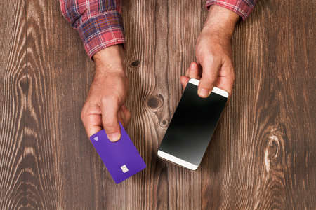 Man holding a credit card and a smartphone on a wooden table