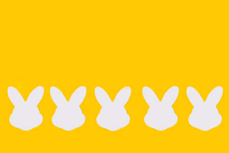White paper rabbit heads on a yellow background with copy space