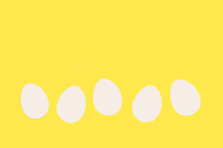 White paper eggs on a yellow background with copy spaceの写真素材