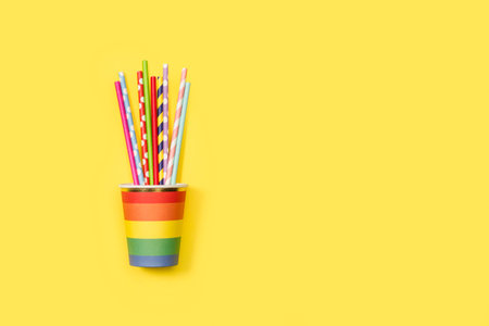 Colored striped drinking straws in a colored disposable glass on a yellow background with copy spaceの写真素材