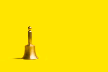 A bronze bell on a yellow background with copy spaceの写真素材