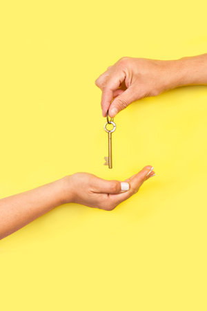 Man hand giving a key to a woman hand on a yellow background with copy space