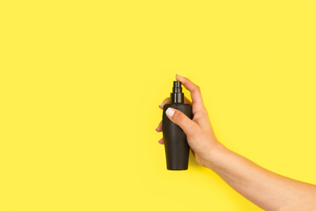 Woman hand holding a perfume sprayer on a yellow background with copy spaceの写真素材