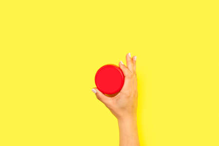 Woman hand holding a red round plastic lid on a yellow background with copy spaceの写真素材