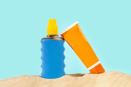 Orange and blue suntan lotion bottle on the sand and on a blue backgroundの写真素材