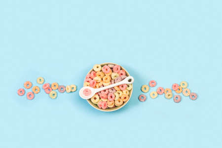 Fruit flavor colored cereals in a bowl on a light blue background with copy space